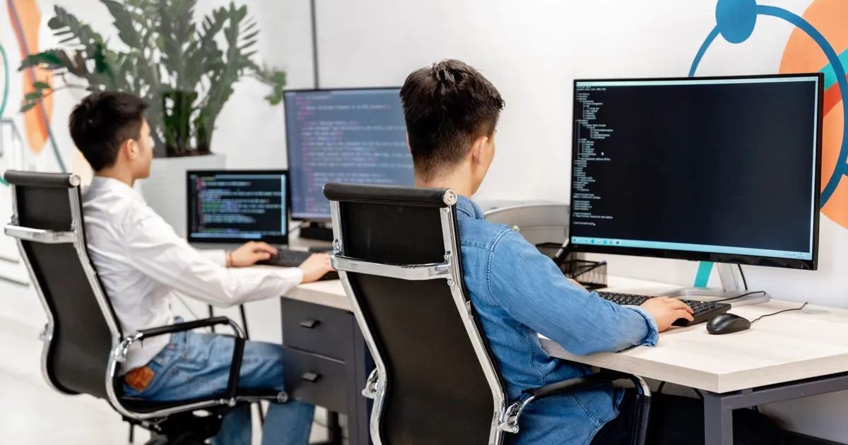 Two DevOps engineers coding at workstations with large monitors